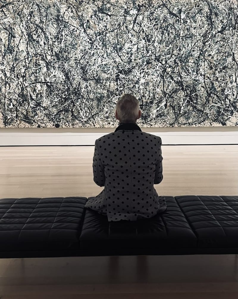 Gene Seidman seated on a museum bench, viewed from behind, studying a large abstract expressionist painting