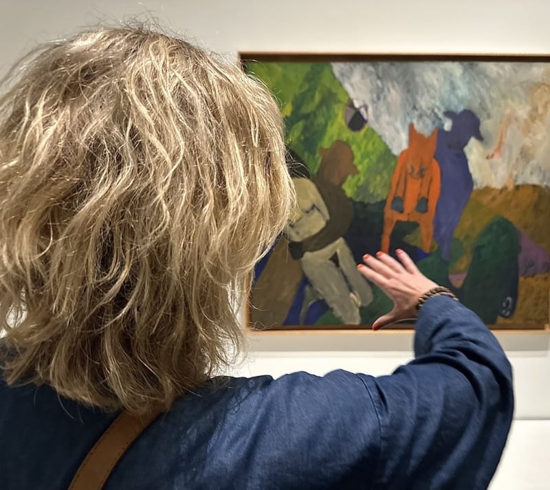 Woman in a blue jacket pointing at a colorful figurative painting on a museum gallery wall